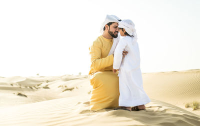 Couple standing on beach against clear sky