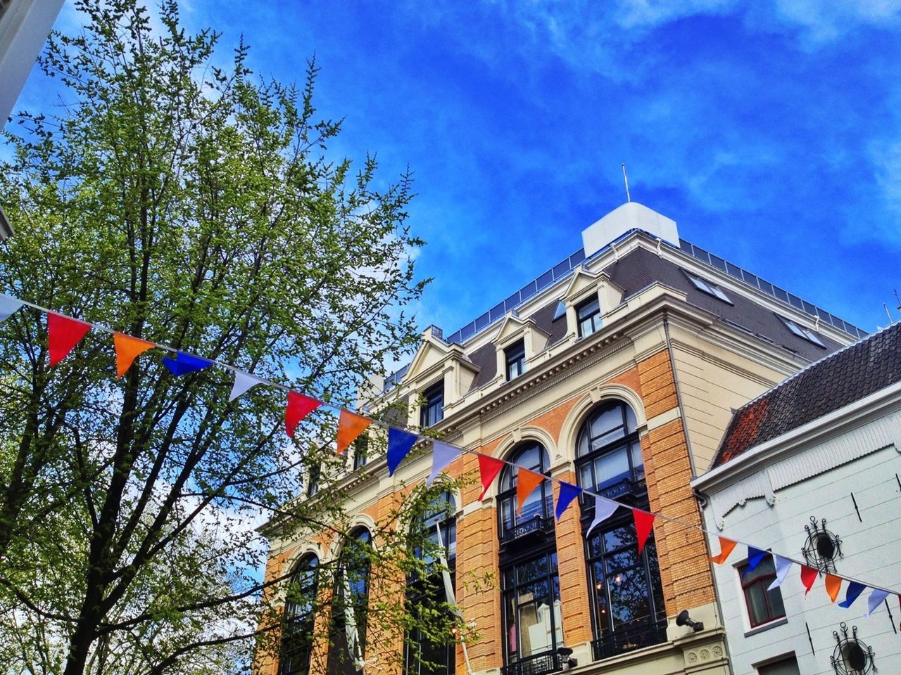 architecture, low angle view, building exterior, built structure, sky, tree, blue, place of worship, religion, church, spirituality, day, outdoors, building, cloud, no people, flag, window