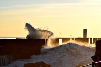 Waves splashing on shore against sky during sunset