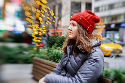 Young woman looking away while standing outdoors during winter