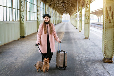 Beautiful young casual tourist woman with dog and suitcase waiting for train