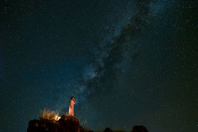 Low angle view of woman standing on cliff against sky at night