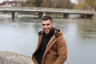 Portrait of smiling man standing on bridge over river during winter