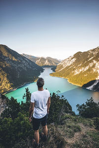 Rear view of man standing on mountain by sea against clear sky