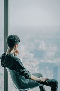 Rear view of man sitting on chair while looking through window