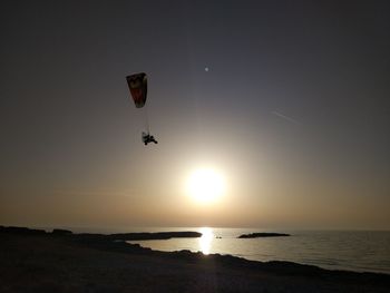 People paragliding over sea against sky during sunset