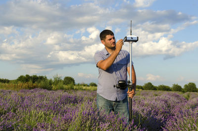 Surveyor examining equipment amidst lavender field against sky