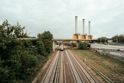 Railroad tracks by factory against sky