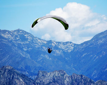 Person paragliding over mountains against sky