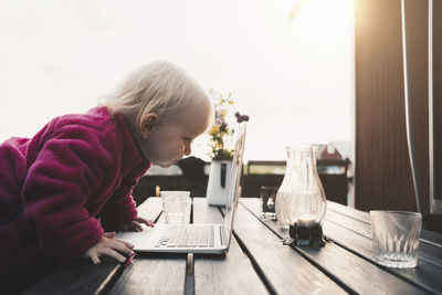 Side view of girl looking at laptop on table in holiday villa against clear sky