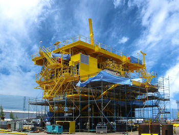 Low angle view of yellow crane by building against sky