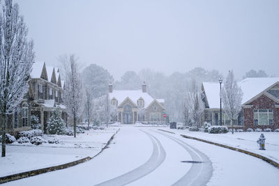 Snow covered road by buildings against sky