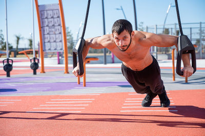 Shirtless man doing loop exercises outdoors. 