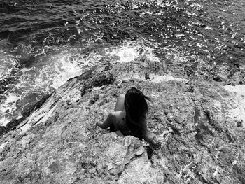 High angle rear view of woman sitting on rock by sea