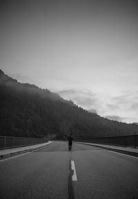 Mid distant view of man walking on bridge towards mountain against sky