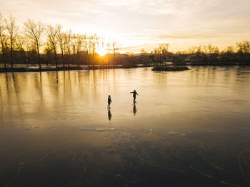 Friends skating on frozen pond during sunset