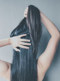 Rear view of woman holding hair against wall