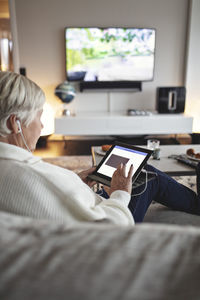 Senior woman using digital tablet while sitting on sofa in living room