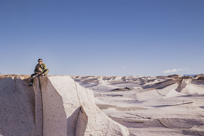 Scenic view of man and baby sitting on rock against clear blue sky