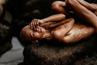 Low section of shirtless women sitting on rock