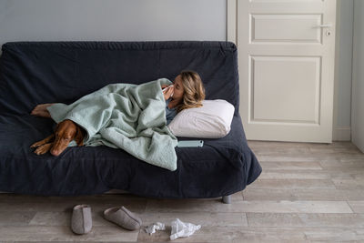 Full length of sick woman relaxing on sofa with dog at home