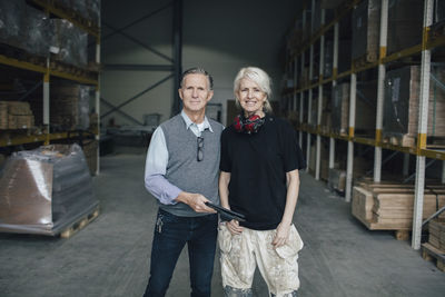 Portrait of smiling business colleagues standing against racks at industry