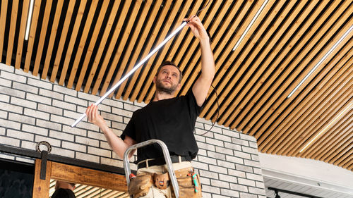 An electrician installs low voltage led lamps in a plank ceiling. builder assembles loft ceiling.