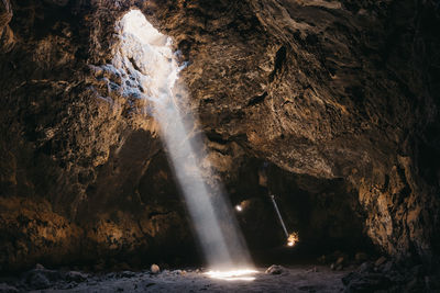 Light beams pierce through the dark volcanic cave