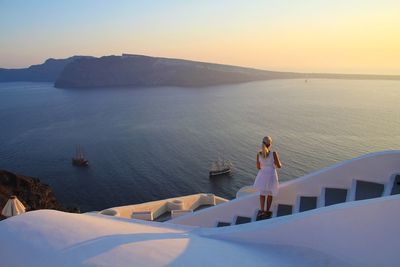 Rear view of woman standing on steps against sea during sunset