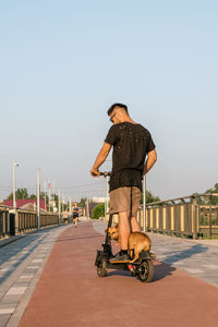 Man is riding on electric scooter with his small dog. walking with dog on empty street of city. 