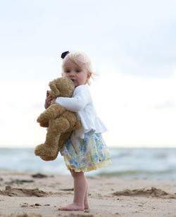 Full length portrait of baby girls with toy at beach against sky