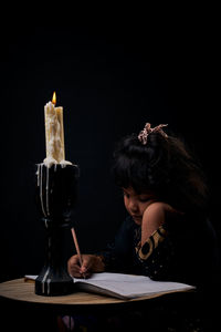 Woman looking at camera while sitting on table against black background