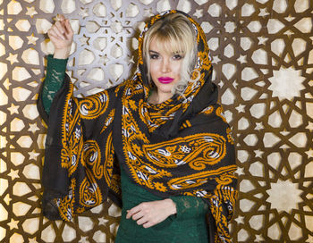 Portrait of woman wearing scarf standing against wall