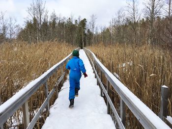 Rear view of boy running on snow covered boardwalk in forest