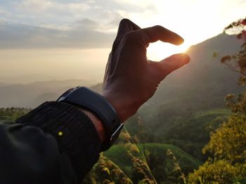 Midsection of man holding sun against sky during sunset