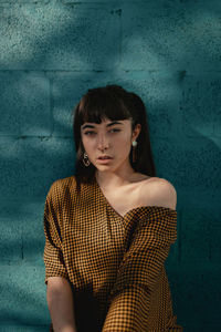 Portrait of a young woman sitting against wall