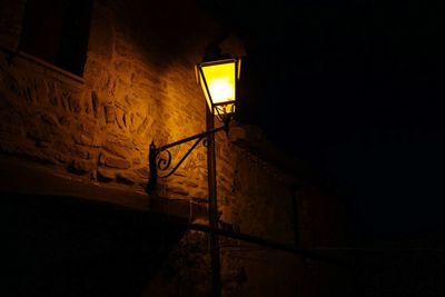 Low angle view of illuminated gas light by wall at night