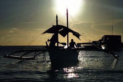 Silhouette people on sailboat at sea against sky during sunset