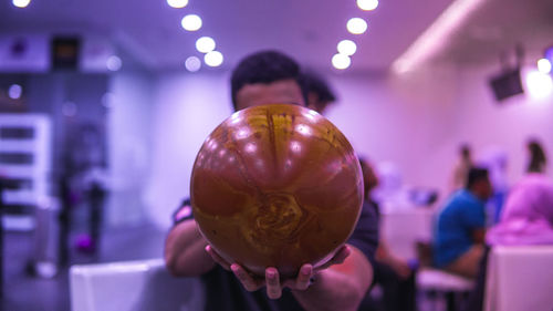 Man holding ball over face against illuminated purple lights