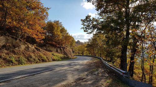 Road amidst trees against sky during autumn