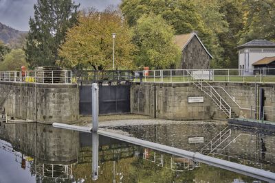 Built structure by lake against trees and buildings