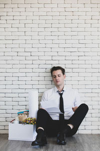 Portrait of young man sitting against wall