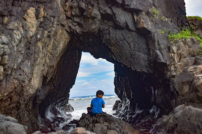 Rear view of man on rock by sea