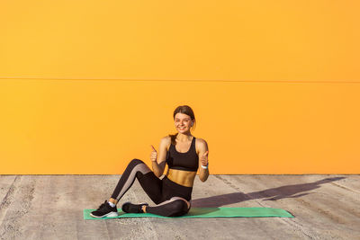 Portrait of woman sitting against yellow wall