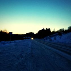 Snow covered road against clear sky during sunset