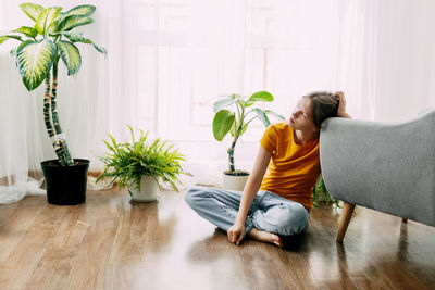 A thoughtful girl sits on the floor in a room and looks into the distance