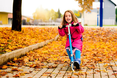 Portrait of girl riding push scooter at park during autumn