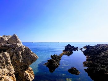 Rock formation in sea against clear blue sky