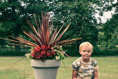 Portrait of boy standing by plants against trees