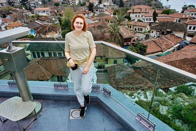 Portrait of smiling young woman standing against buildings